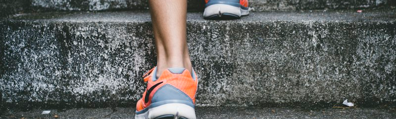 Scarpe da corsa arancioni su un muretto di pietra, pronte per una corsa nel parco